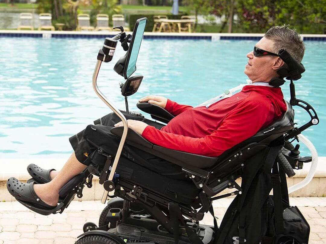 Homme atteint de la maladie de Charcot et en fauteuil roulant électrique devant une piscine